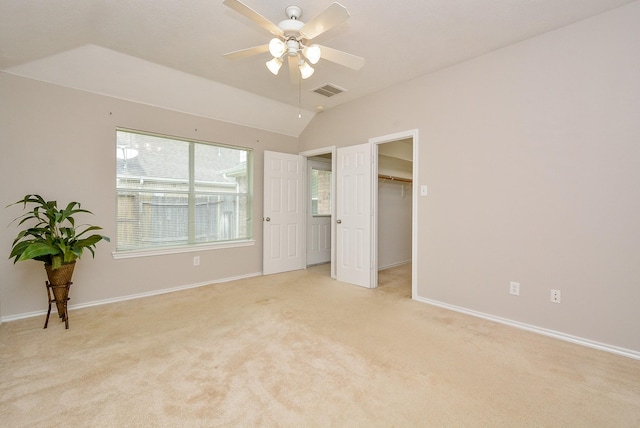 unfurnished bedroom featuring a walk in closet, lofted ceiling, light colored carpet, and ceiling fan