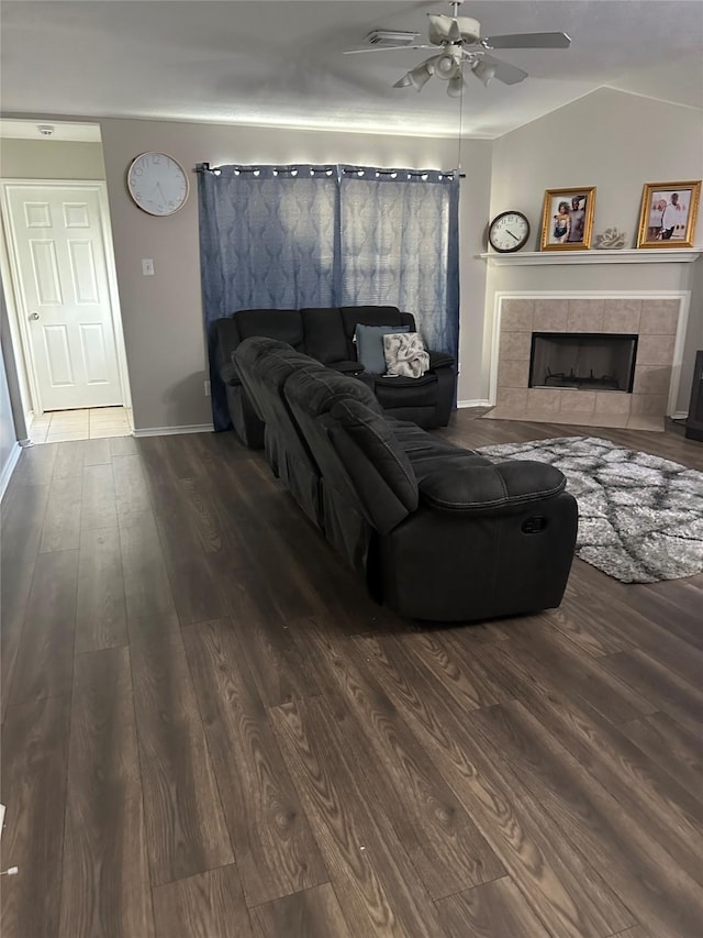 living room featuring a tiled fireplace, vaulted ceiling, dark hardwood / wood-style floors, and ceiling fan