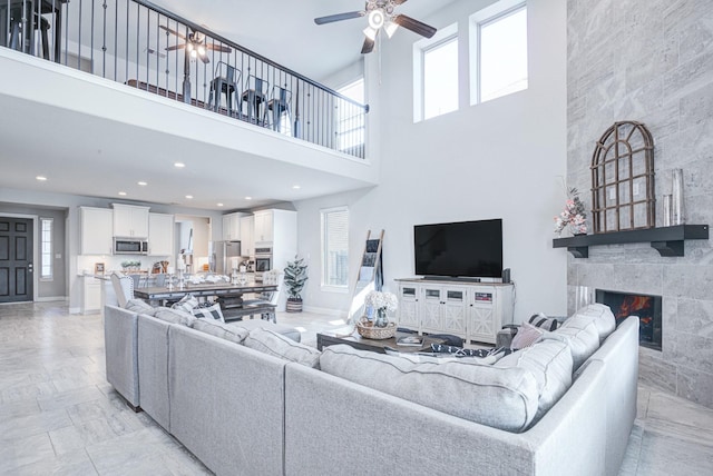 living room with a tiled fireplace, a wealth of natural light, and ceiling fan