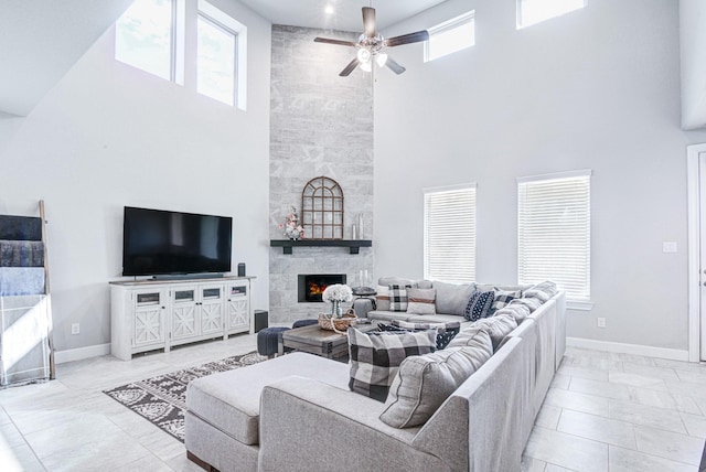 living room with ceiling fan, a large fireplace, plenty of natural light, and a towering ceiling