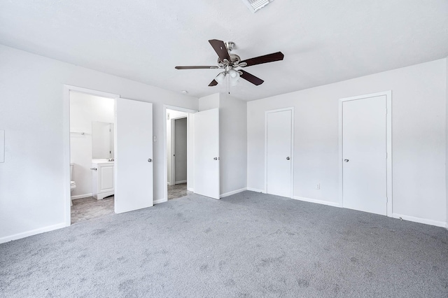 unfurnished bedroom featuring multiple closets, ensuite bathroom, carpet, and ceiling fan