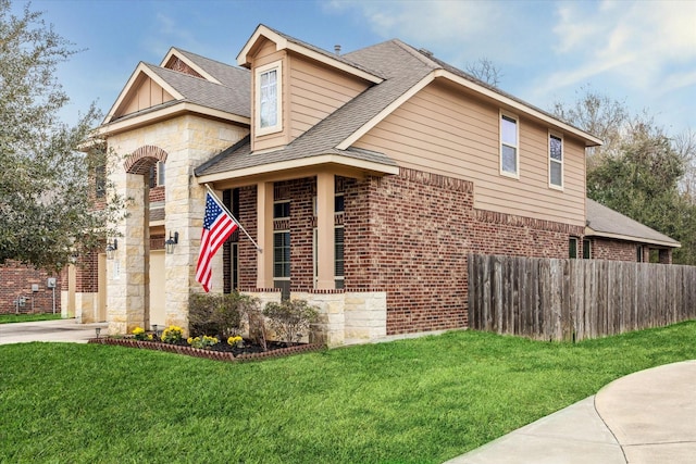 view of front facade with brick siding, a shingled roof, fence, driveway, and a front yard