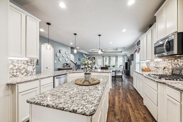 kitchen with appliances with stainless steel finishes, decorative light fixtures, a center island, light stone counters, and kitchen peninsula