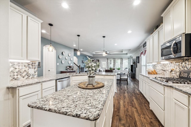 kitchen featuring ceiling fan, a kitchen island, open floor plan, a peninsula, and stainless steel appliances