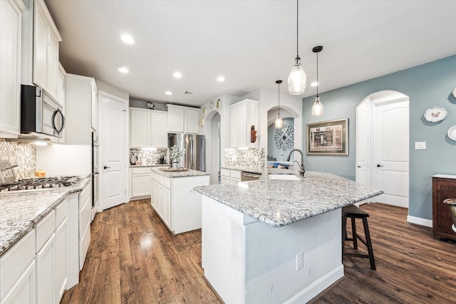 kitchen with a sink, arched walkways, stainless steel appliances, and dark wood-style flooring