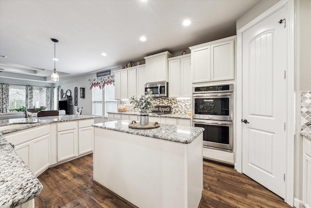 kitchen featuring white cabinetry, a center island, appliances with stainless steel finishes, pendant lighting, and light stone countertops