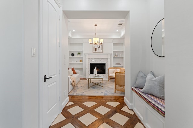 living room featuring crown molding, built in shelves, a fireplace, and a raised ceiling