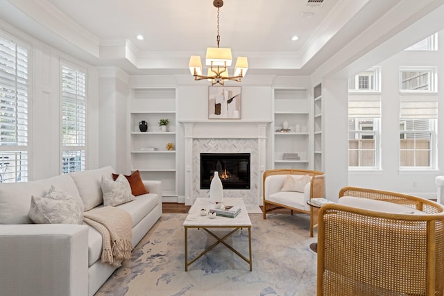 living room featuring ornamental molding, built in features, a high end fireplace, and a tray ceiling