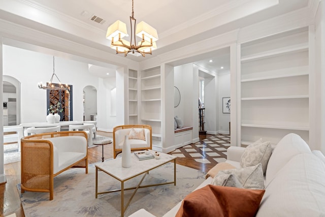 living room with built in shelves, ornamental molding, a tray ceiling, a notable chandelier, and hardwood / wood-style flooring