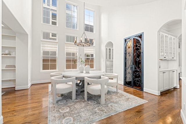 dining area with a high ceiling, hardwood / wood-style floors, an inviting chandelier, and built in shelves