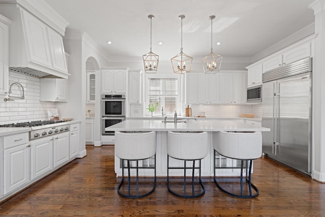 kitchen featuring built in appliances, a kitchen island with sink, and white cabinets