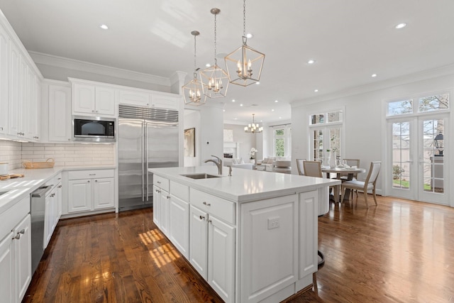 kitchen with pendant lighting, white cabinetry, an island with sink, sink, and built in appliances