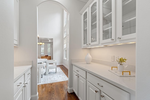 bar featuring white cabinetry, light stone counters, dark wood-type flooring, and an inviting chandelier