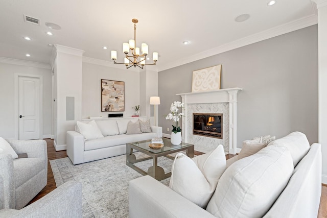 living room featuring an inviting chandelier, crown molding, a high end fireplace, and light hardwood / wood-style floors