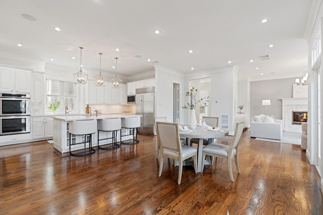 dining area with a fireplace, sink, crown molding, dark wood-type flooring, and an inviting chandelier