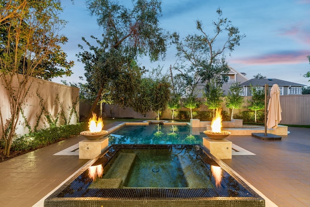 pool at dusk featuring an in ground hot tub, a patio area, and a fire pit