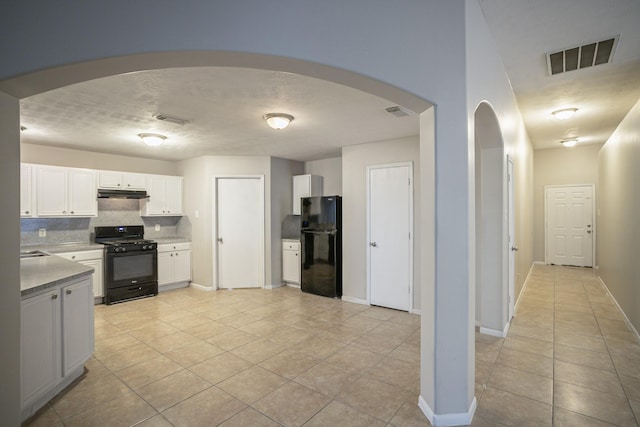 kitchen with tasteful backsplash, white cabinetry, light tile patterned floors, black appliances, and a textured ceiling