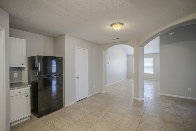 kitchen featuring light tile patterned flooring, white cabinetry, a textured ceiling, black refrigerator, and decorative backsplash