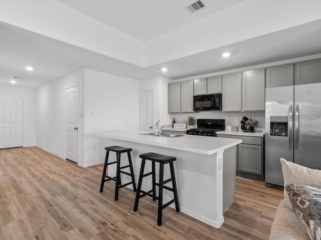 kitchen with sink, gray cabinetry, black appliances, a center island with sink, and light wood-type flooring