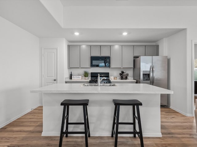 kitchen with an island with sink, sink, gray cabinetry, and light hardwood / wood-style flooring