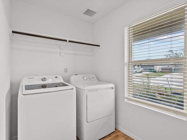 laundry area featuring independent washer and dryer, wood-type flooring, and a wealth of natural light