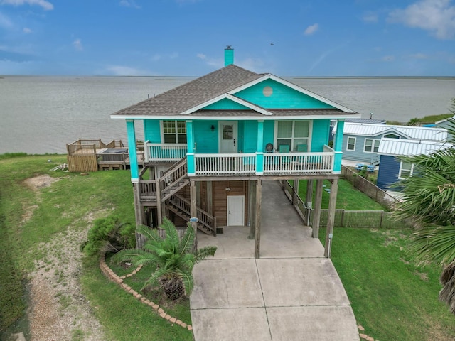 raised beach house featuring a carport, a water view, covered porch, and a front lawn