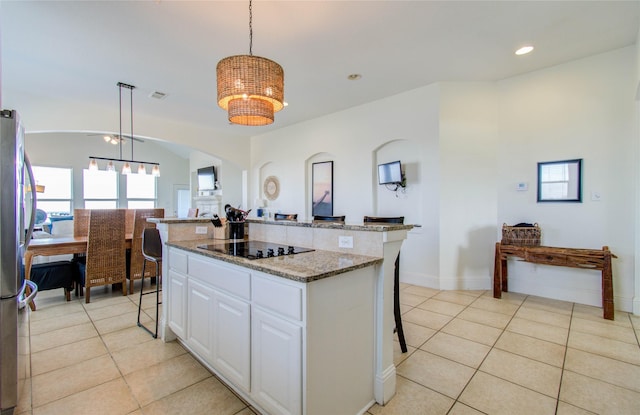 kitchen with a kitchen island, white cabinets, hanging light fixtures, black electric stovetop, and light stone countertops