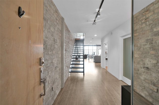 hall featuring expansive windows, track lighting, brick wall, and light hardwood / wood-style floors