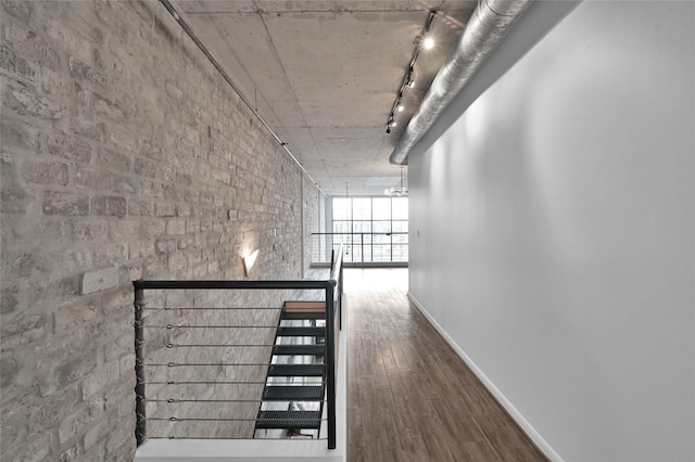 corridor with brick wall, wood-type flooring, and rail lighting