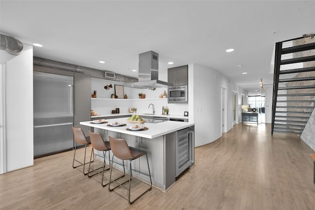 kitchen featuring gray cabinets, a breakfast bar, built in appliances, wine cooler, and island exhaust hood