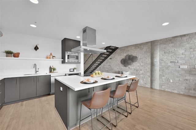 kitchen featuring sink, a breakfast bar area, gray cabinetry, appliances with stainless steel finishes, and island exhaust hood