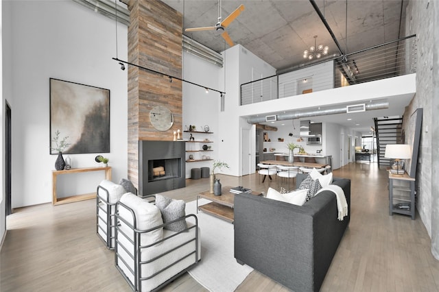 living room featuring a towering ceiling, a fireplace, a chandelier, and light wood-type flooring