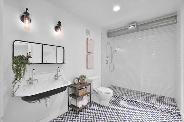 bathroom with tiled shower, sink, and toilet