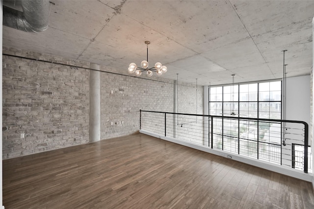 unfurnished room featuring hardwood / wood-style flooring, brick wall, and a notable chandelier