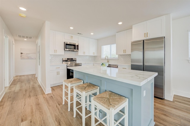 kitchen with a breakfast bar, white cabinetry, light stone counters, a center island, and appliances with stainless steel finishes