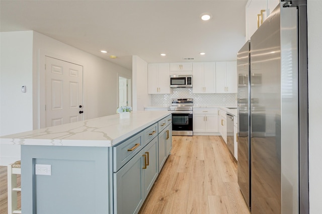 kitchen with appliances with stainless steel finishes, white cabinetry, backsplash, a kitchen island, and light wood-type flooring