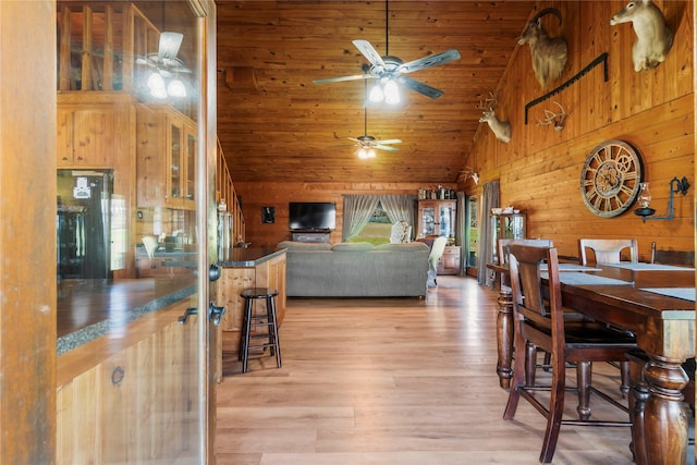 dining space featuring wood walls, light hardwood / wood-style floors, ceiling fan, high vaulted ceiling, and wood ceiling