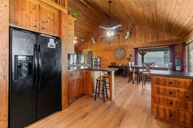 kitchen featuring kitchen peninsula, wood ceiling, light hardwood / wood-style floors, wooden walls, and black fridge