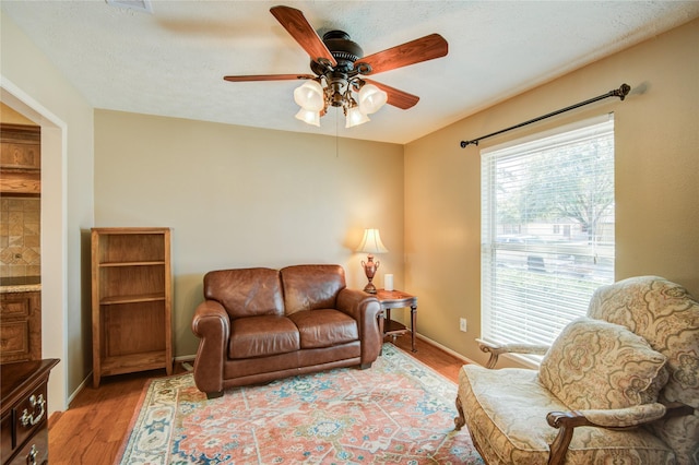 living room with a textured ceiling, ceiling fan, and light hardwood / wood-style flooring