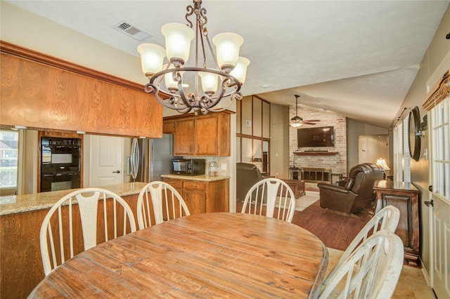 dining area with a brick fireplace, ceiling fan with notable chandelier, and vaulted ceiling