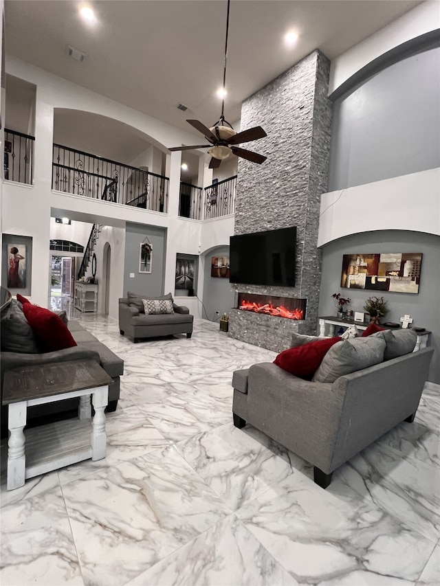 living room featuring ceiling fan, a fireplace, and a high ceiling