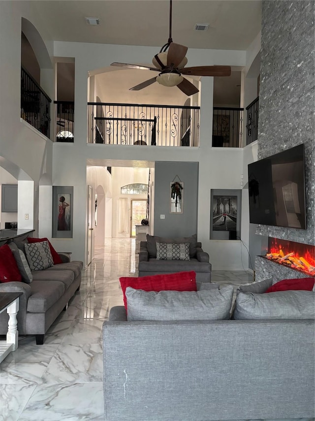 living room featuring a towering ceiling, a fireplace, and ceiling fan