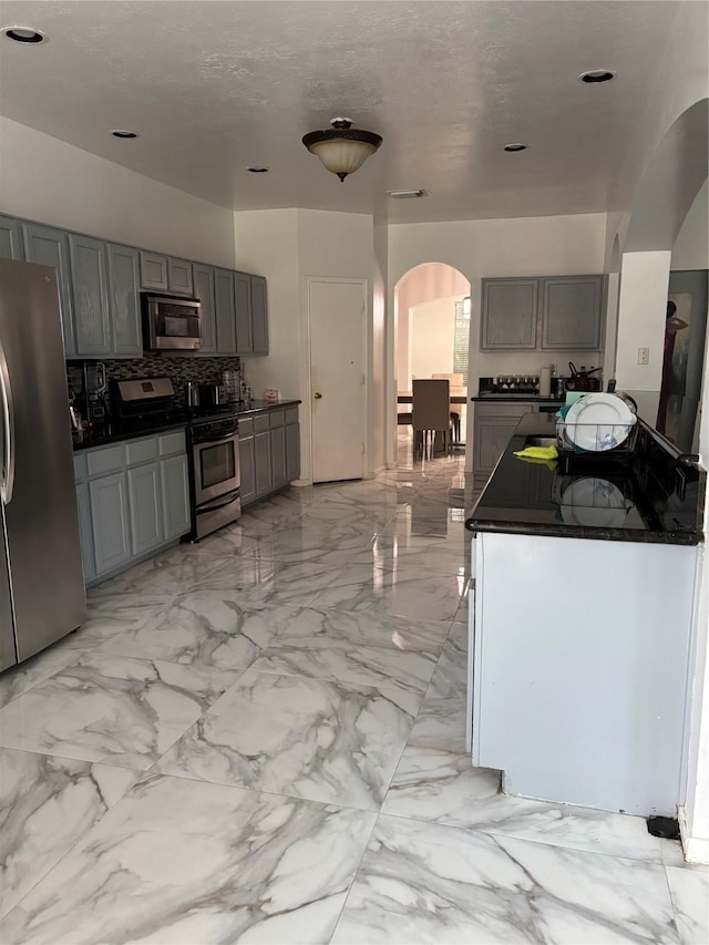 kitchen with gray cabinetry, decorative backsplash, stainless steel appliances, and a textured ceiling