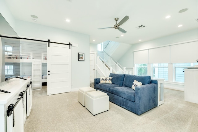 living room with ceiling fan, a barn door, and light carpet