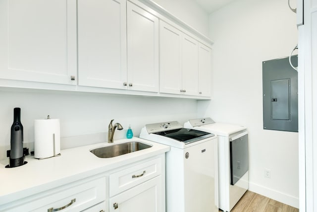 clothes washing area featuring sink, cabinets, electric panel, washer and clothes dryer, and light hardwood / wood-style flooring