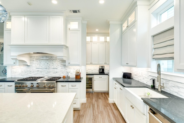 kitchen with wine cooler, sink, white cabinetry, appliances with stainless steel finishes, and dark stone counters