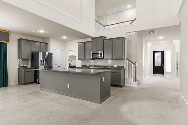 kitchen with sink, gray cabinetry, a kitchen island with sink, stainless steel appliances, and dark stone counters