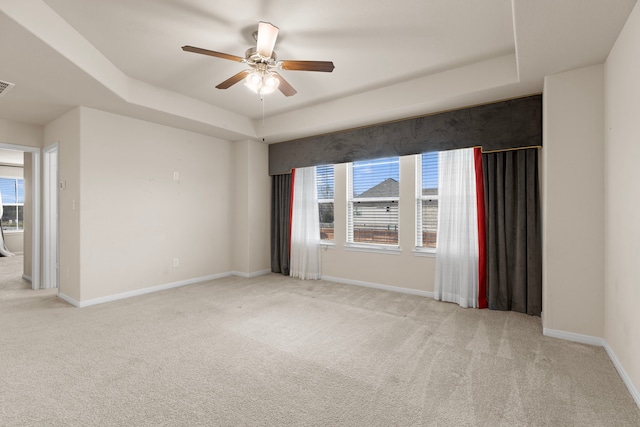 carpeted spare room featuring ceiling fan, plenty of natural light, and a tray ceiling