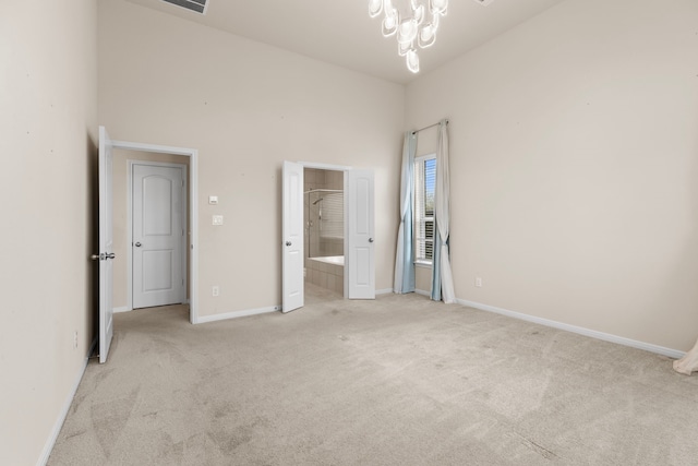 unfurnished bedroom featuring a towering ceiling, ensuite bathroom, a chandelier, and light carpet