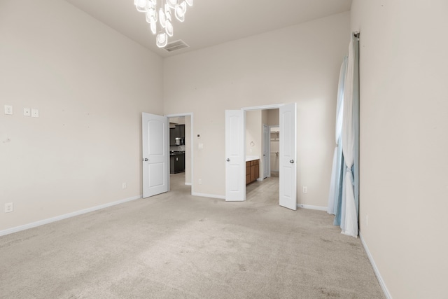 unfurnished bedroom featuring a towering ceiling, ensuite bathroom, light carpet, and a notable chandelier